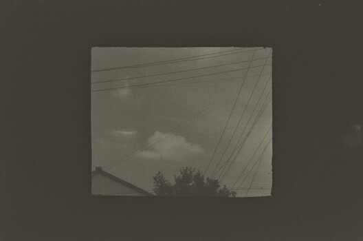 Overexposed photograph viewed through window showing power lines and cloudy sky