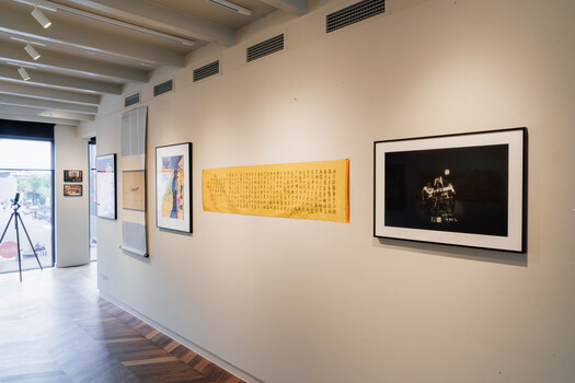Gallery wall displaying framed artwork and photographs in a bright, minimalist exhibition space