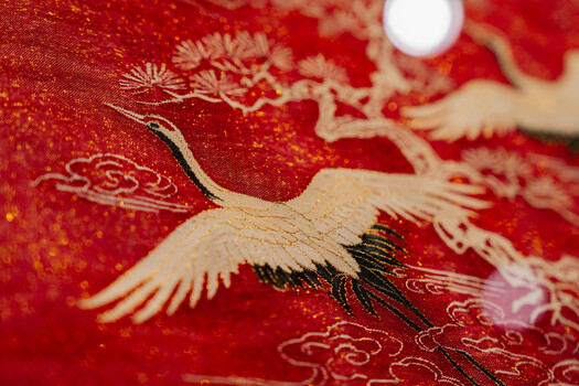 Embroidered crane with spread wings on red fabric with gold thread details