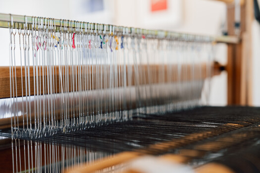 Weaving loom with numerous vertical threads and colored markers indicating pattern placement