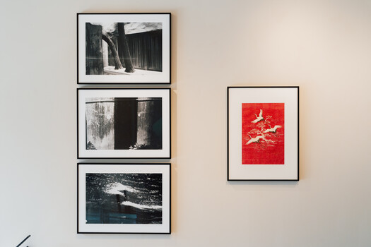 Gallery wall with three black-framed black and white photographs on left and one red framed artwork on right