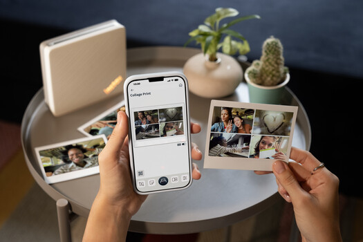 Hands holding smartphone and printed photos over desk with plants and photo printing supplies