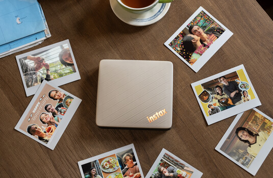 Instax printer surrounded by instant film prints arranged on wooden surface