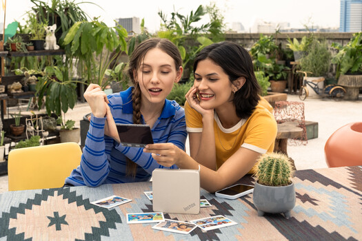 Two women reviewing content on a tablet on a rooftop garden surrounded by potted plants