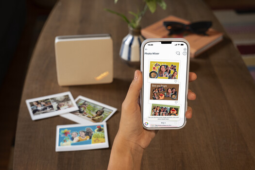 Hand holding smartphone displaying photo gallery app with printed photos scattered on wooden table