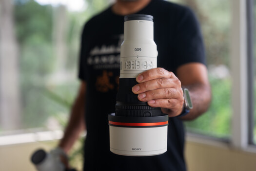 Photographer holding a Sony telephoto lens with white barrel and orange accent ring