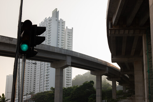 Green traffic light mounted on pole with elevated highway interchange and residential high-rises in background