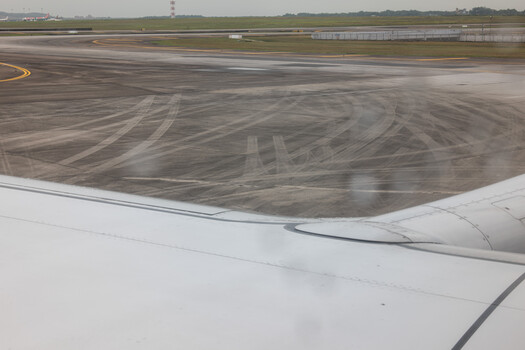 Aerial view from airplane window showing airport runway with tire marks and taxiway patterns