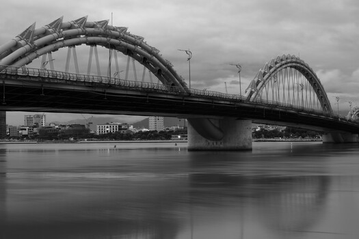 Architectural bridge with dramatic curved steel arches spanning calm water under overcast sky