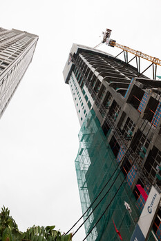 Upward perspective of modern high-rise building under construction with green safety netting and crane.