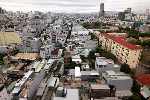 Aerial cityscape showing dense urban residential buildings with mountains in the distance under overcast sky