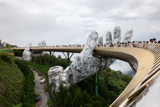 Giant stone hands emerge from lush jungle, supporting a curved wooden footbridge