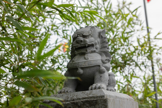 Stone lion statue on pedestal partially obscured by green foliage