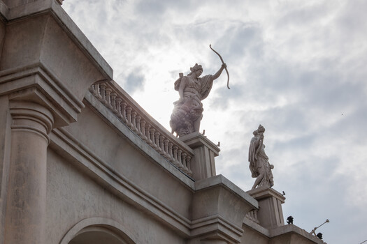 Neoclassical roofline statues against cloudy sky with ornate cornice details