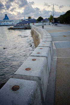 Waterfront promenade with concrete bollards leading toward moored boats and cloudy sky