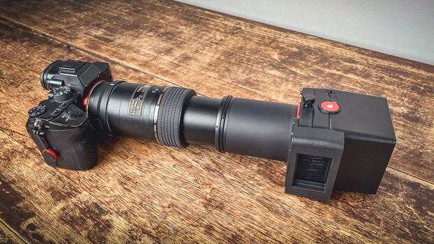 Camera with telephoto lens attached to external monitor mounted on wooden surface
