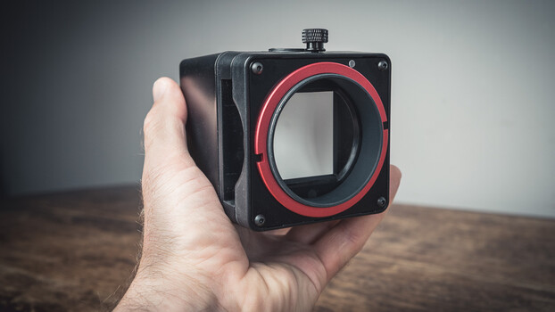 Hand holding a compact cinema camera with red lens mount and black body
