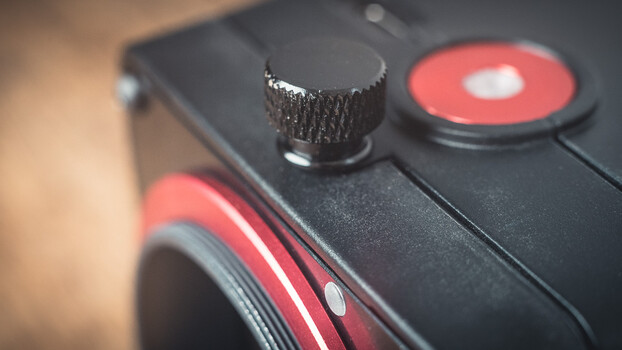 Close-up of a camera's control dial with textured metal knob and red accent ring