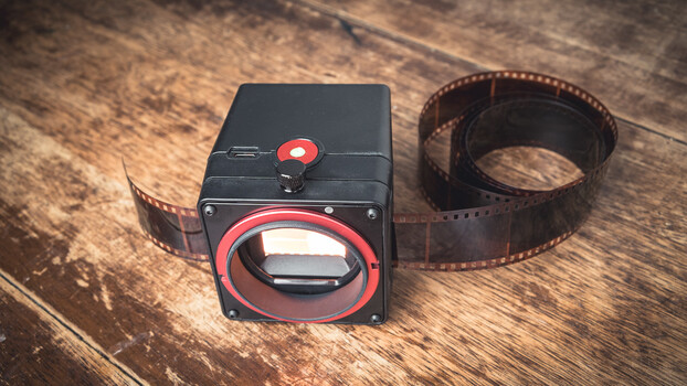 Medium format film camera with red accents and film strip on wooden surface