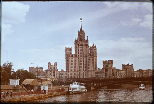 Stalinist architecture building with distinctive tower reflected in Moscow River with boats