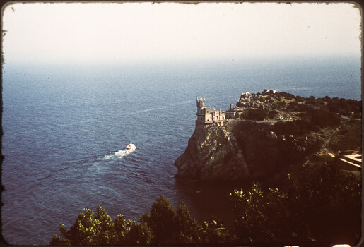 Clifftop castle overlooking Mediterranean sea with small boat in water