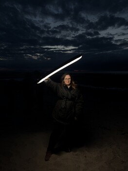 Person holding a glowing light trail against a dramatic twilight sky