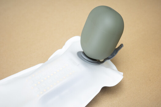 White mannequin arm displaying a gray silicone ear prosthetic against a neutral tan background