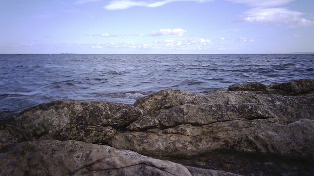 Rocky coastline with calm sea and blue sky with scattered clouds
