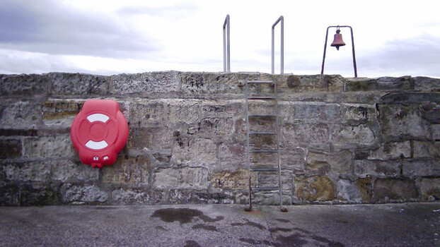 Red life preserver mounted on weathered stone fortification wall with metal structures
