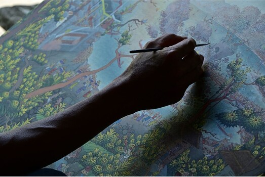 Artist's hand holding a brush, painting detailed foliage on an illustrated landscape