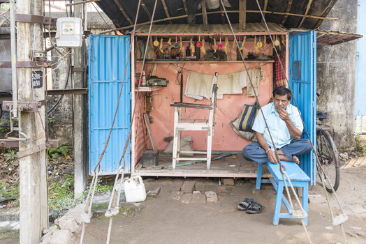 Man sitting in a modest blue and coral street-side repair shop with tools and hanging meat