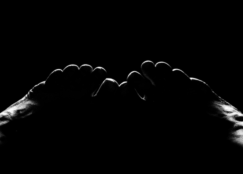 Silhouetted hands forming a heart shape against black background with rim lighting