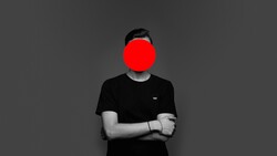 Person in black t-shirt with arms crossed, face obscured by large red circle.