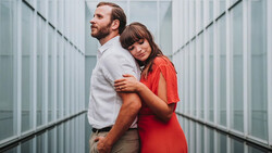 Couple posing together in a modern corridor with symmetrical glass and metal walls.