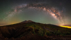 Milky Way arcing over a volcanic mountain silhouette at night.
