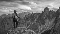 Hiker with backpack and trekking poles standing on a rocky ridge overlooking dramatic jagged peaks.