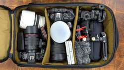Open camera equipment case with DSLR body, lenses, microphone, audio recorder, and accessories organized in padded compartments.
