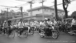 Large group of people on bicycles and motorcycles gathered on a wide street in an urban area.