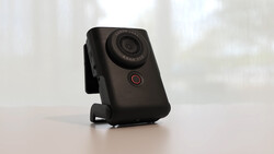 Black compact camera with red power button mounted on white surface against blurred background.