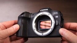 Canon EOS R8 mirrorless camera held in two hands with sensor exposed, shown against a brown gradient background.