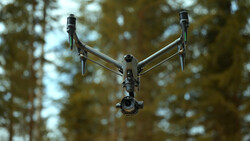 DJI Inspire 3 drone hovering against a blurred forest canopy backdrop.