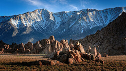 Distinctive rock formations in desert valley with snow-capped mountains in background.