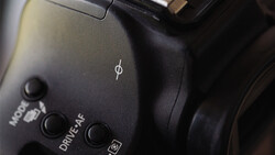 Close-up of camera body controls showing mode dial, drive settings, and ISO button with dramatic side lighting.