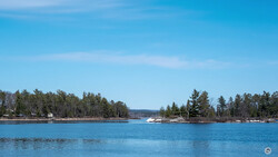 Calm blue lake with forested shoreline and boats under clear sky.