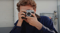 Person holding a Fujifilm rangefinder camera up to their face, preparing to take a photograph.