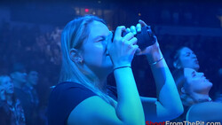 Woman singing into microphone at concert with blue stage lighting and crowd in background.