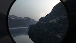 Alpine lake and snow-capped mountains viewed through a circular lens or scope.