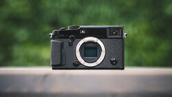 Black mirrorless camera with textured grip displayed against blurred green background.
