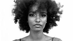 Black and white portrait of a woman with voluminous natural curly hair against a plain background.