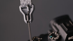 Close-up of a camera strap attachment mechanism with gray fabric strap and metal connector hardware.